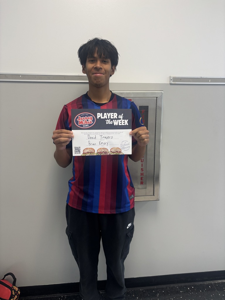 A person holds a check and certificate for Player of the Week in a room with a white wall.