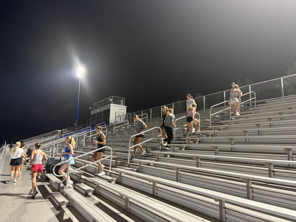 Group of people wearing athletic clothing and sneakers walk up a stadium staircase in the evening.