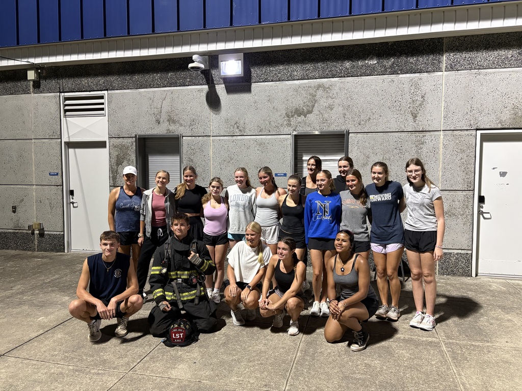 Group of athletes in athletic wear pose for a photo in front of a building.