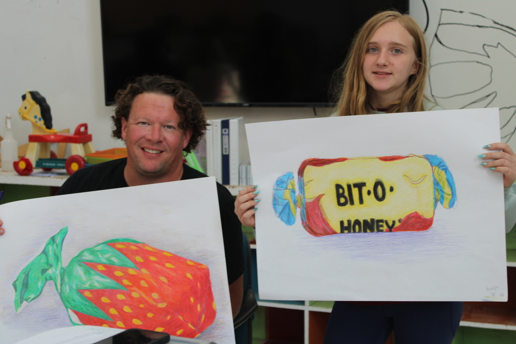 A man and a girl display drawings. The man holds a strawberry drawing. The girl holds a candy drawing labeled "BIT-O HONEY".