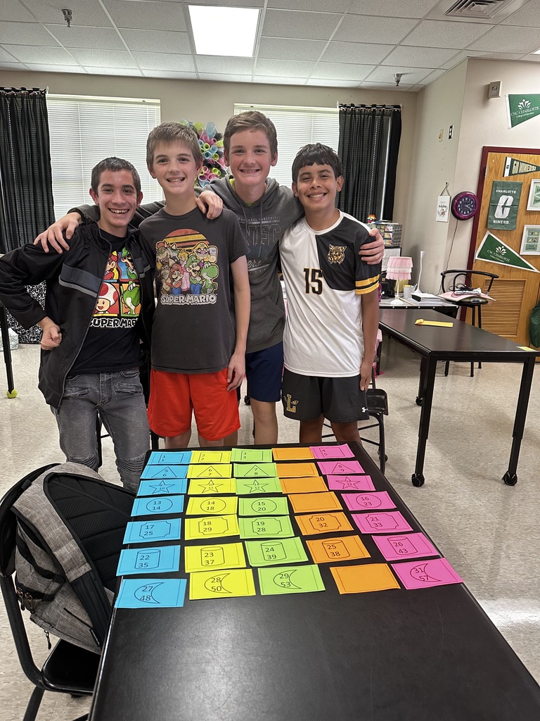 Three boys pose behind a table covered with colorful sticky notes. One boy has his arm around the shoulders of the others.