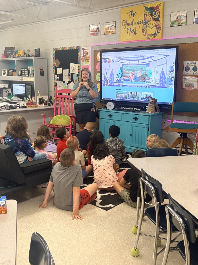 A woman stands in front of a screen showing a cartoon as several young children sit on the floor.