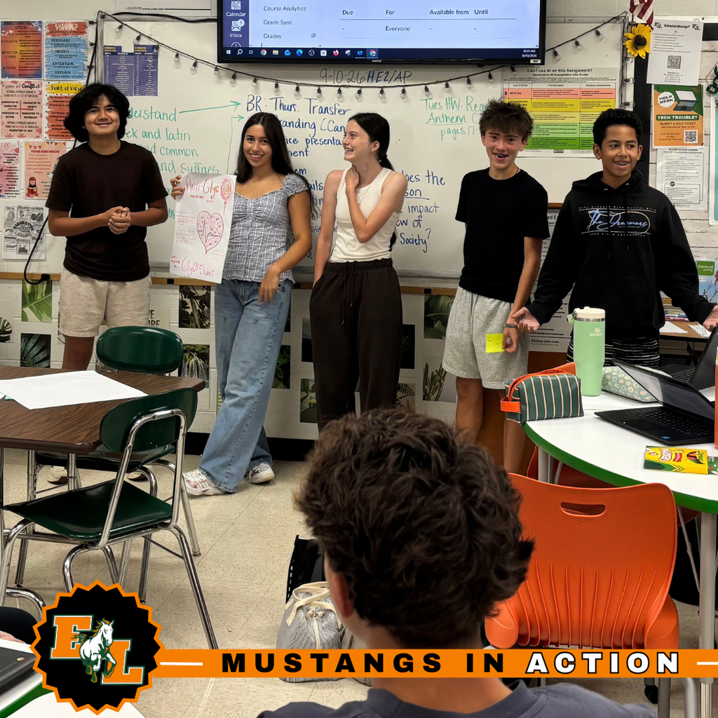 Students in a classroom with a whiteboard and American flag. Four students are standing in front.