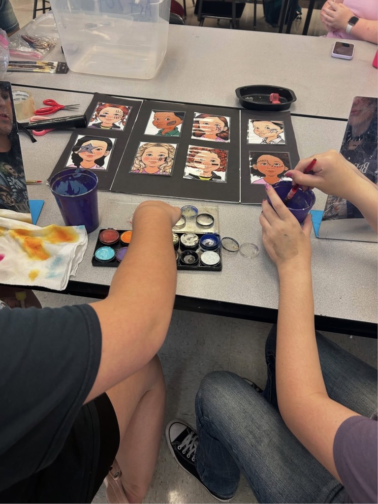 A person mixes paint in a cup while another person paints a portrait on a table.