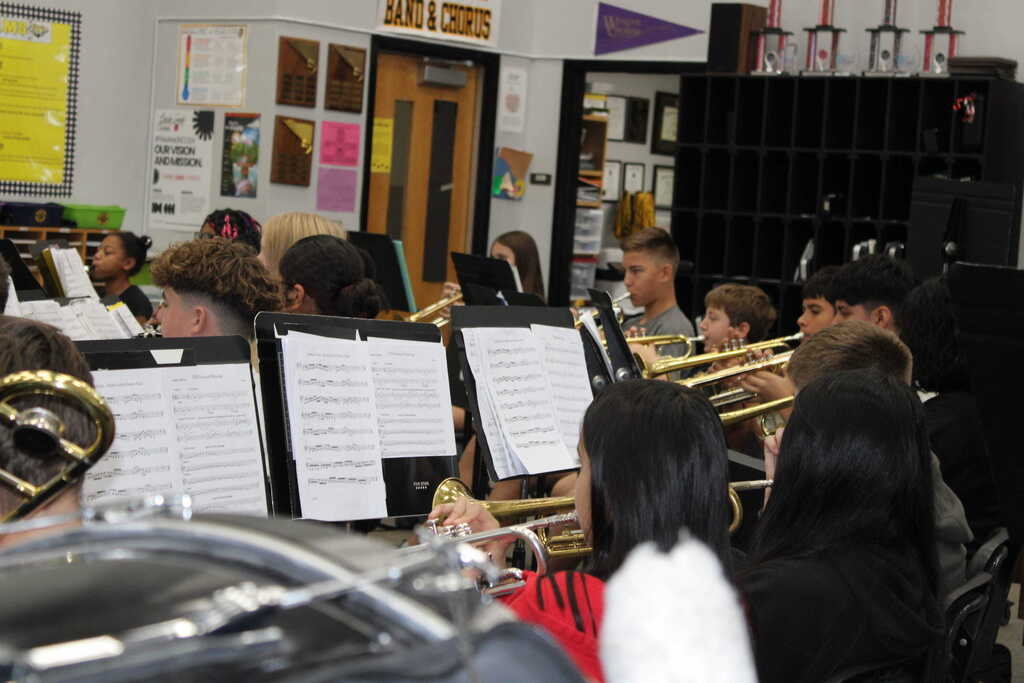 A classroom with several students playing musical instruments. They sit with music stands in front of them.