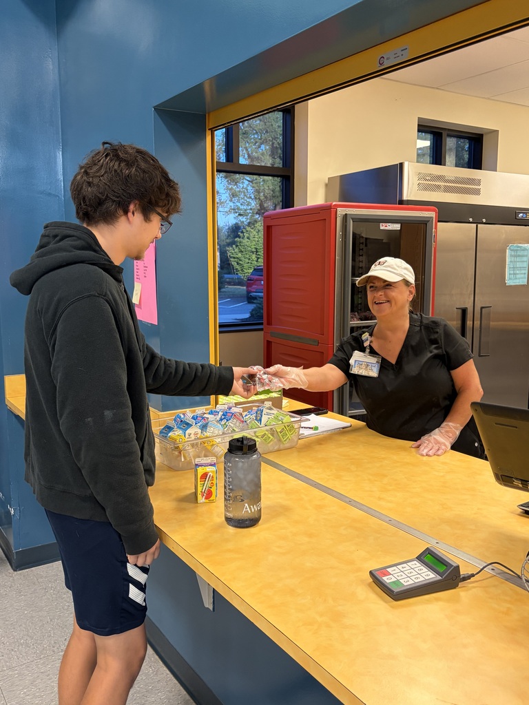 Two people at a counter, one in a hoodie shaking hands with a person in a cap.