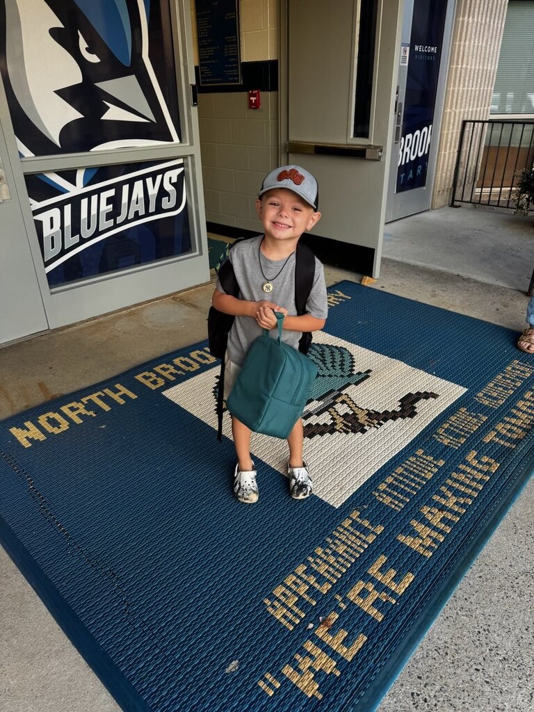 A young boy in a hat stands on a blue rug in front of a building. The rug reads, "We're making tomorrow."