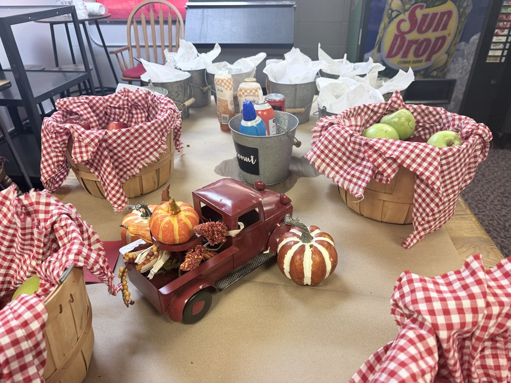 A table holds several baskets with red and white gingham covers. Baskets contain fruit and decorative items. A red toy truck is in the middle.