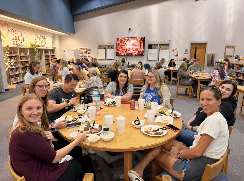 A group of people sitting at a table with plates, cups, and bowls, in a library.