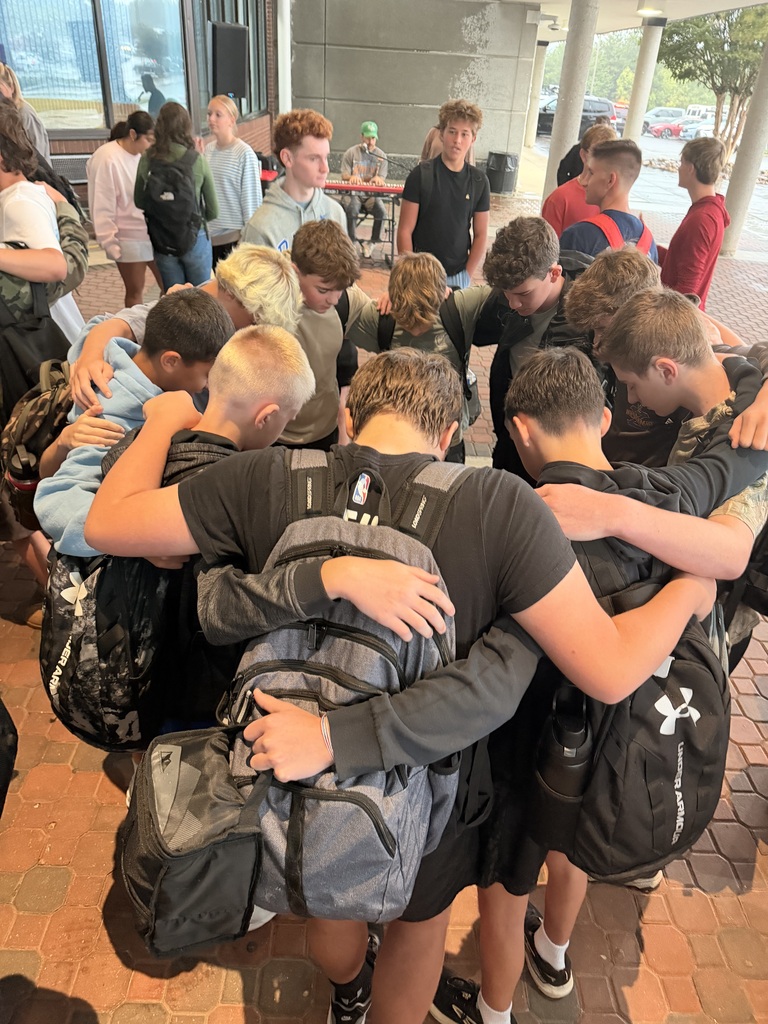 A group of students, wearing backpacks, stand close together with arms around each other in a building.