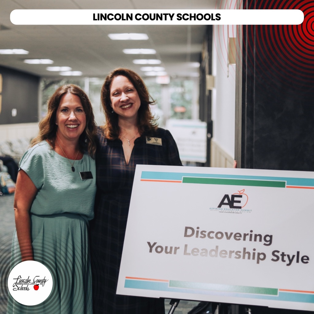 Two women stand next to a sign that says "Discovering Your Leadership Style" in a hallway.