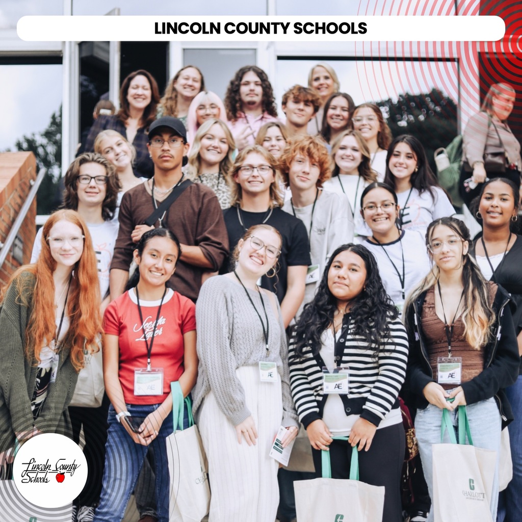 A group of people in various clothing, some wearing ID cards, stand outside Lincoln County Schools.