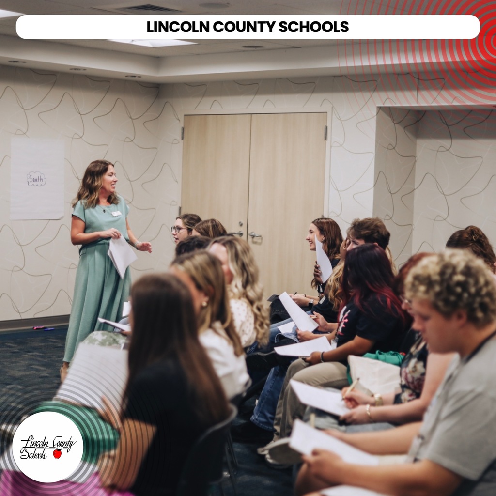 A woman stands in a room with Lincoln County Schools text, presenting to an audience seated in chairs.