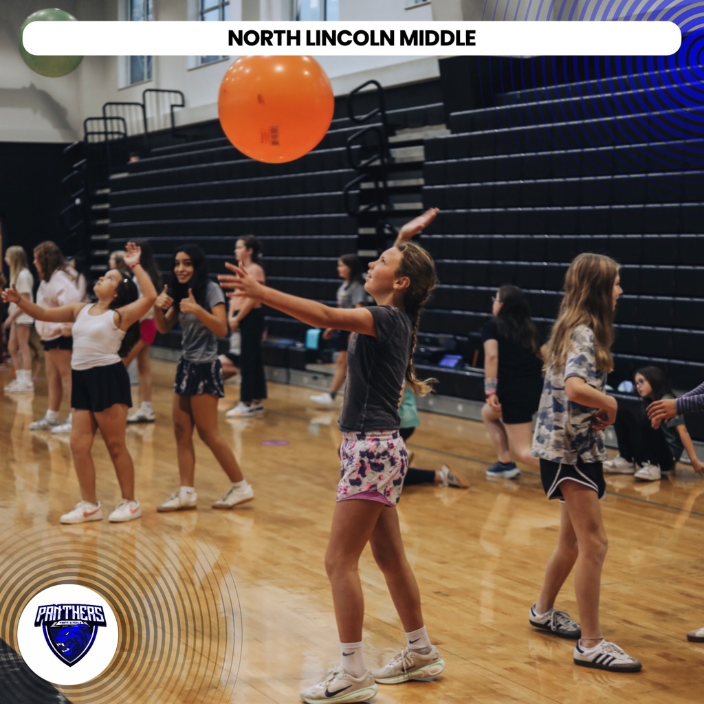 Group of children in a gym, one throwing an orange ball. Background shows bleachers.
