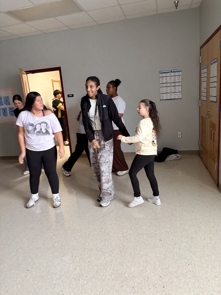 A group of people, including two young girls, walk through a room with white walls and flooring.