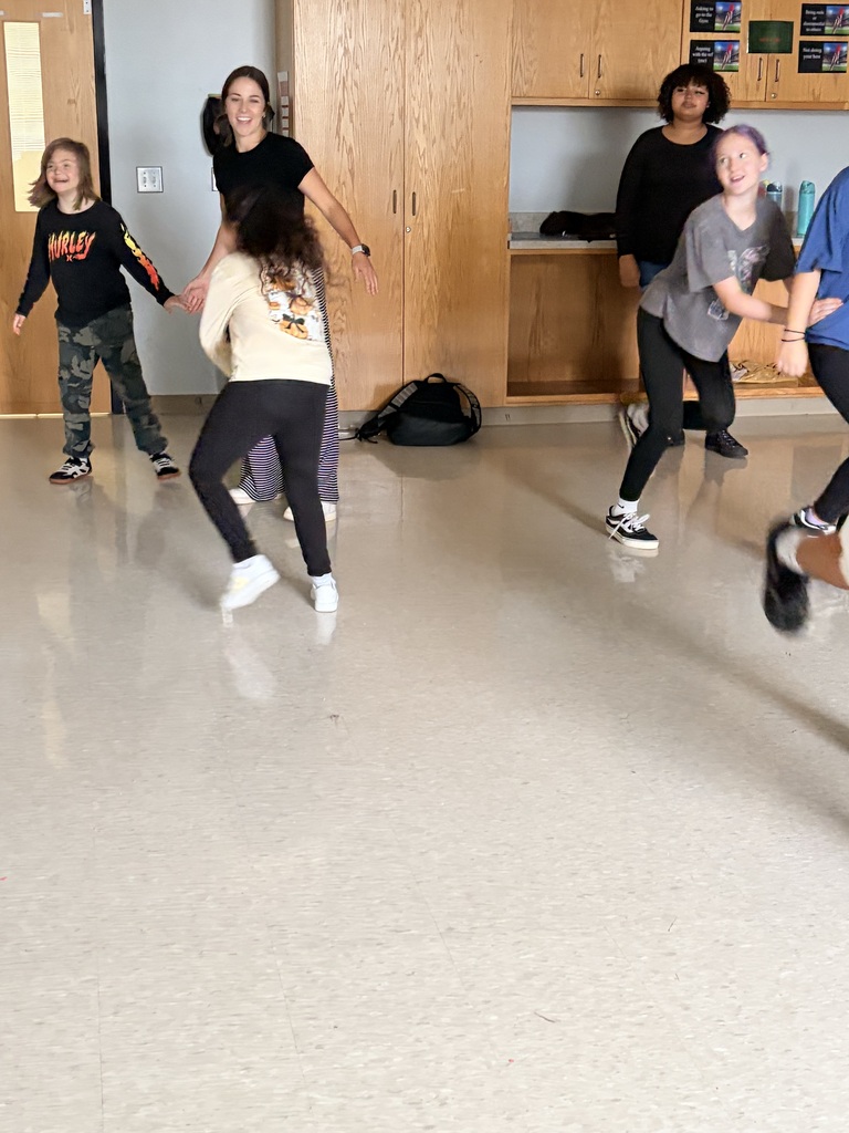 A group of individuals participate in a physical activity within a room with light-colored flooring and wooden cabinets.
