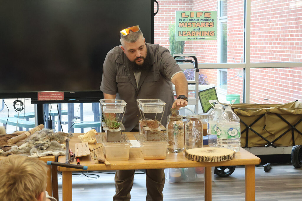 Man standing at a table with various objects, including fish tanks, as a child looks on.