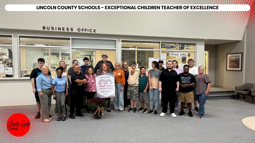 A group of people stands in front of a building, with a sign in the middle.