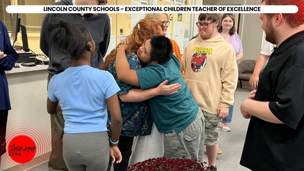 A group of people in a room, some hugging a central person, with a red logo in the bottom left.