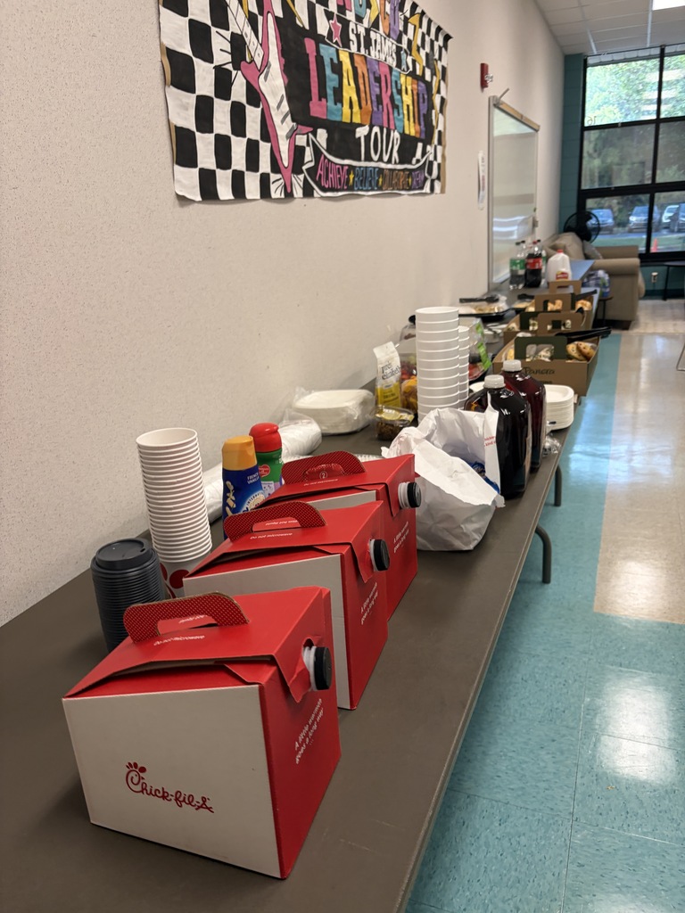 A long table with red boxes, white cups, and bottles. A black and white checkered banner hangs on a wall.
