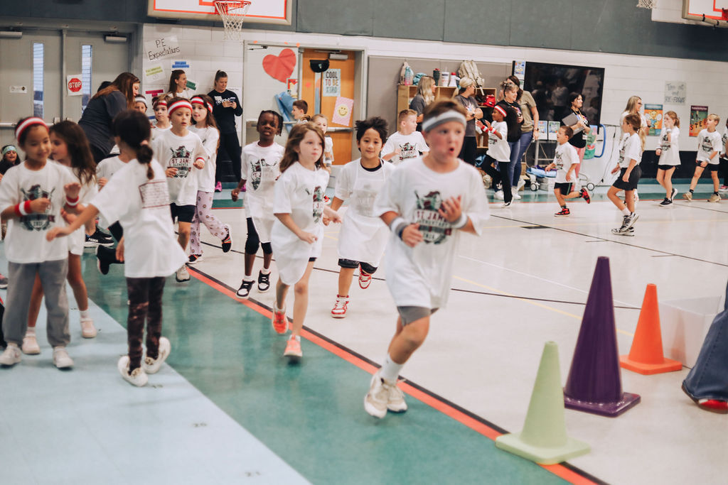 A group of children and a man in white shirts and sneakers running on a basketball court.