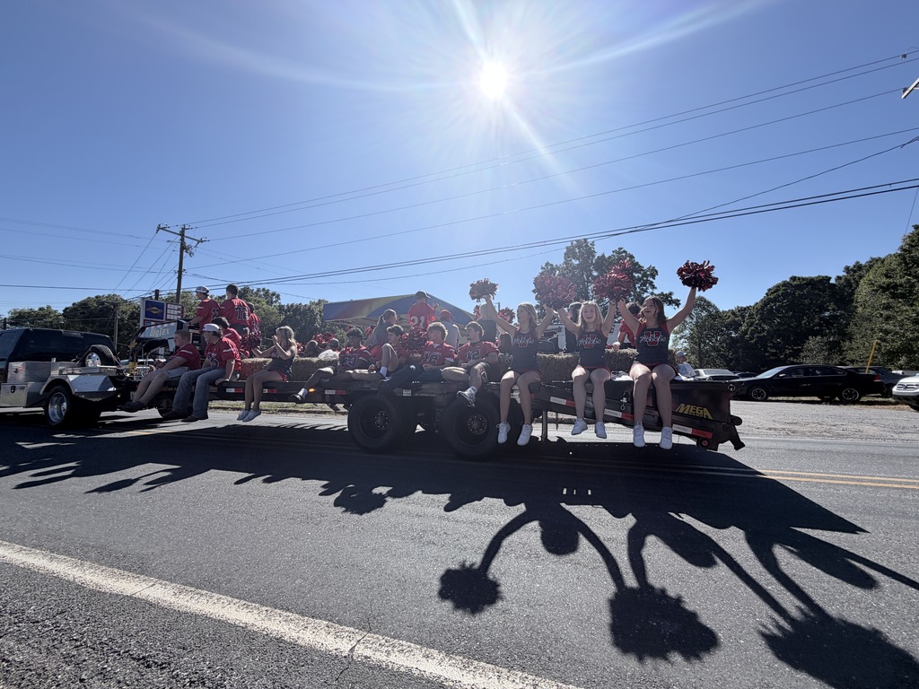 Cheerleaders ride on a trailer in a parade with trees and utility lines in background.