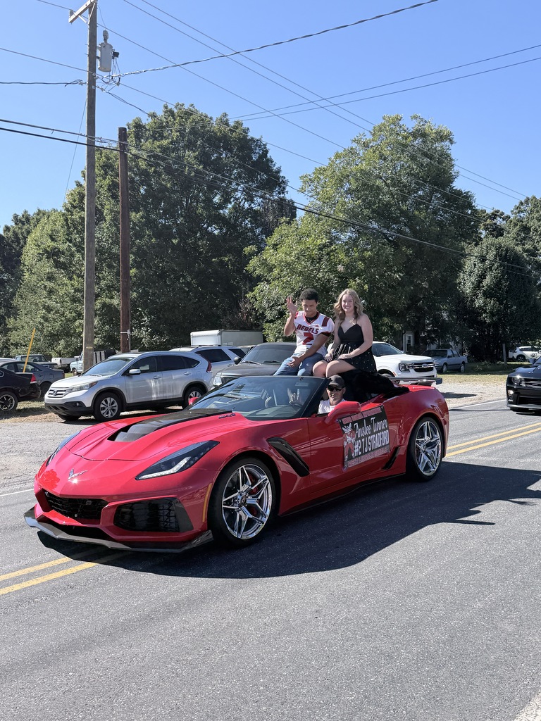 A red sports car with three people on it drives down the street with parked cars in the background.