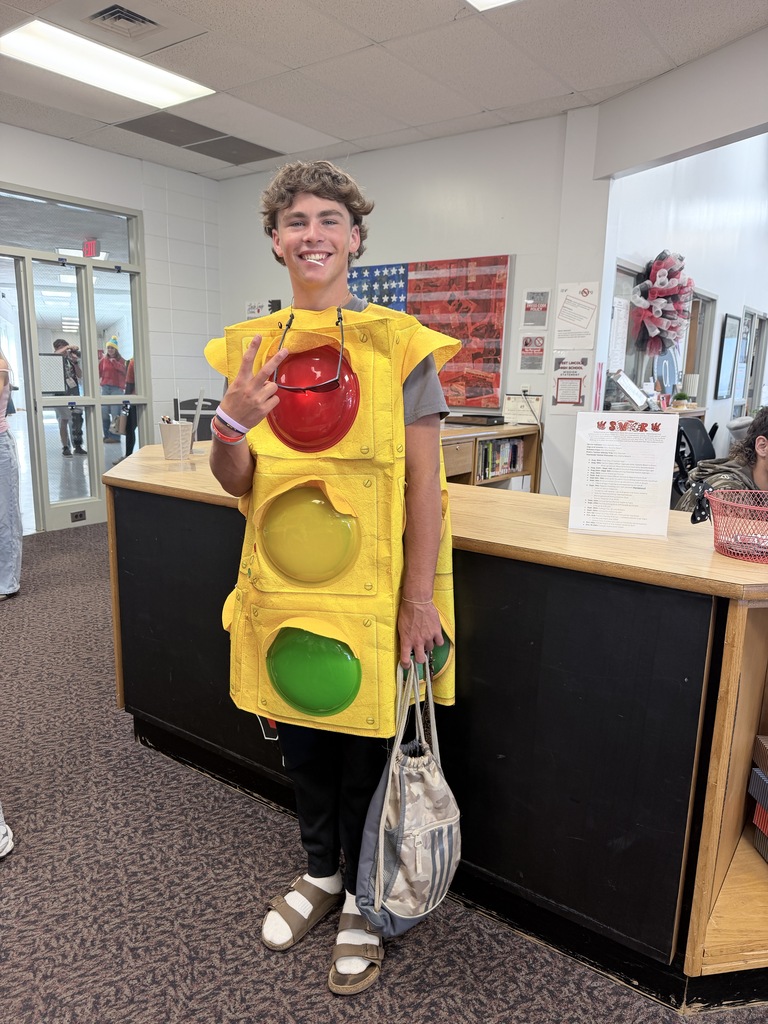 Person wearing a traffic light costume standing by a counter with a peace sign.