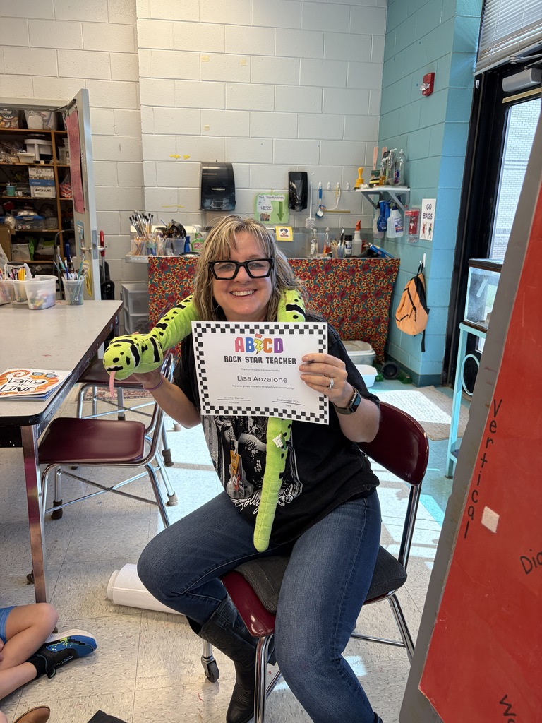 Woman holding a certificate in a classroom, wearing glasses and a black shirt, seated in a chair.