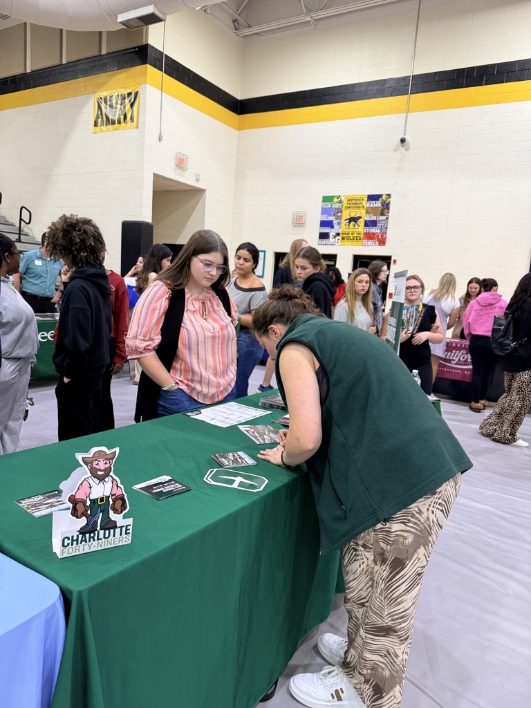 A room with a white ceiling and yellow and black walls. People stand around a table with green tablecloths, cards, and posters.