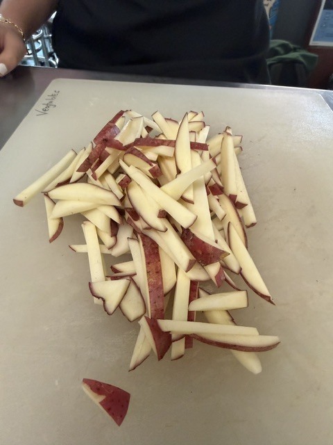 Multiple sliced apple pieces on a white cutting board, with a person's hand partially visible.