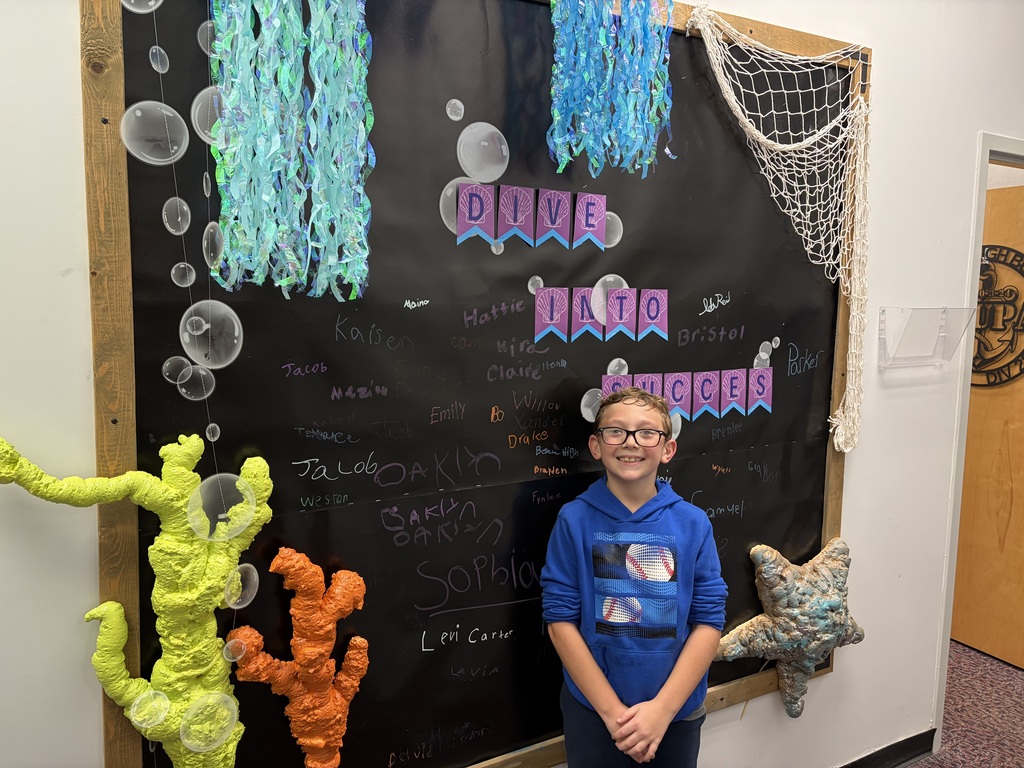 A young person stands in front of a blackboard with ocean-themed decorations and the word "DIVE."