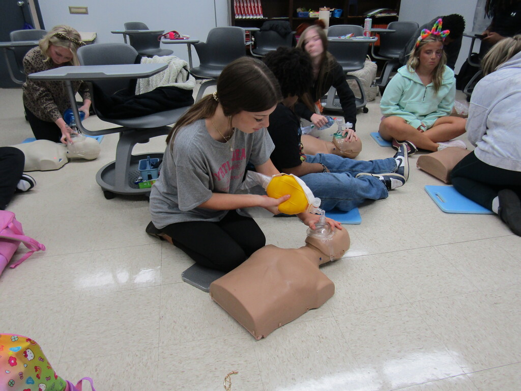 Several young women practicing CPR and first aid on a dummy in a classroom setting.