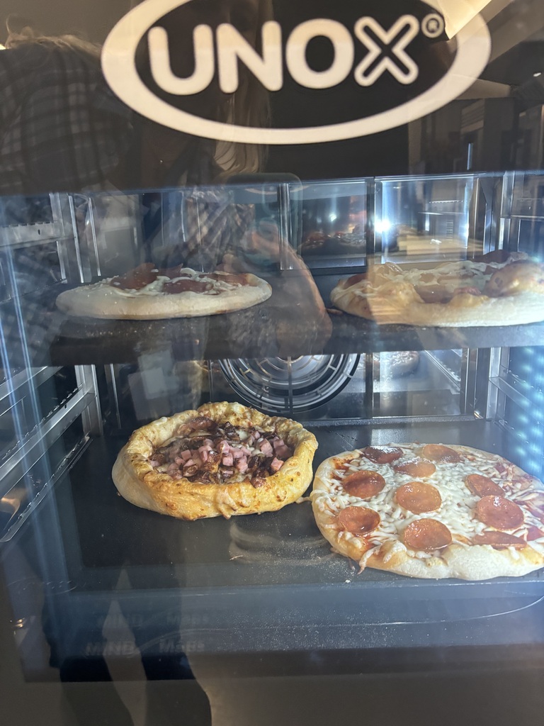 Pizzas on a three-tier display. Pizzas have toppings of pepperoni, sausage, and cheese. "Unox" in white text on black oval.