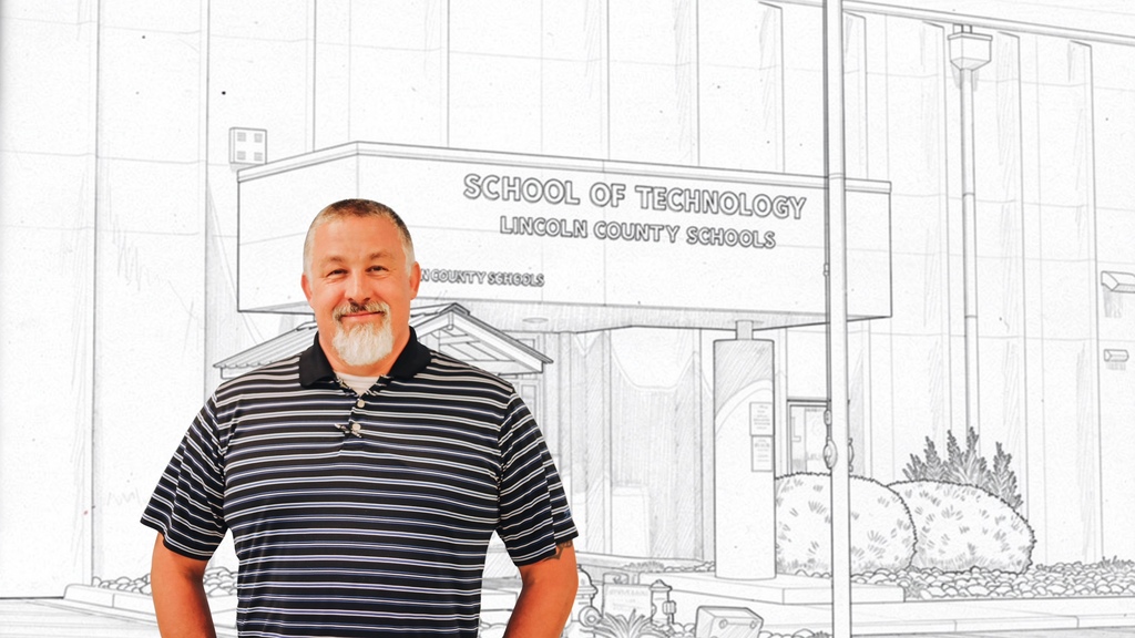 A man with a beard and mustache stands in front of a building with "School of Technology" written on it.