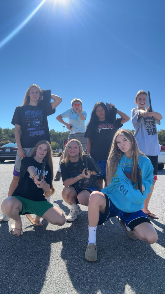 A group of people pose with sunglasses and guitars on a sunny day in a parking lot.
