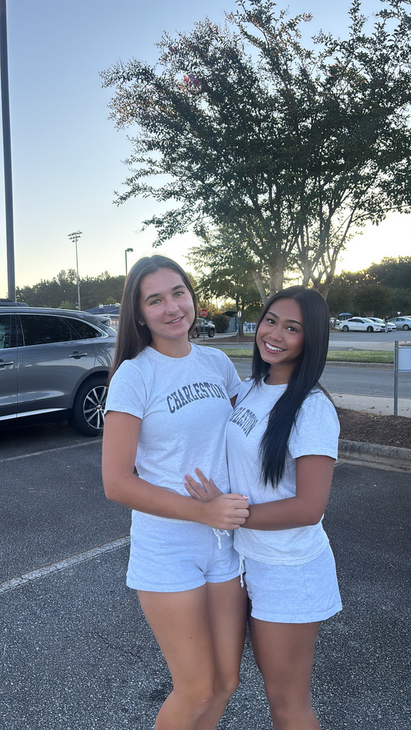 Two women standing in parking lot. One woman has a white shirt and shorts with Charleston printed on the front.