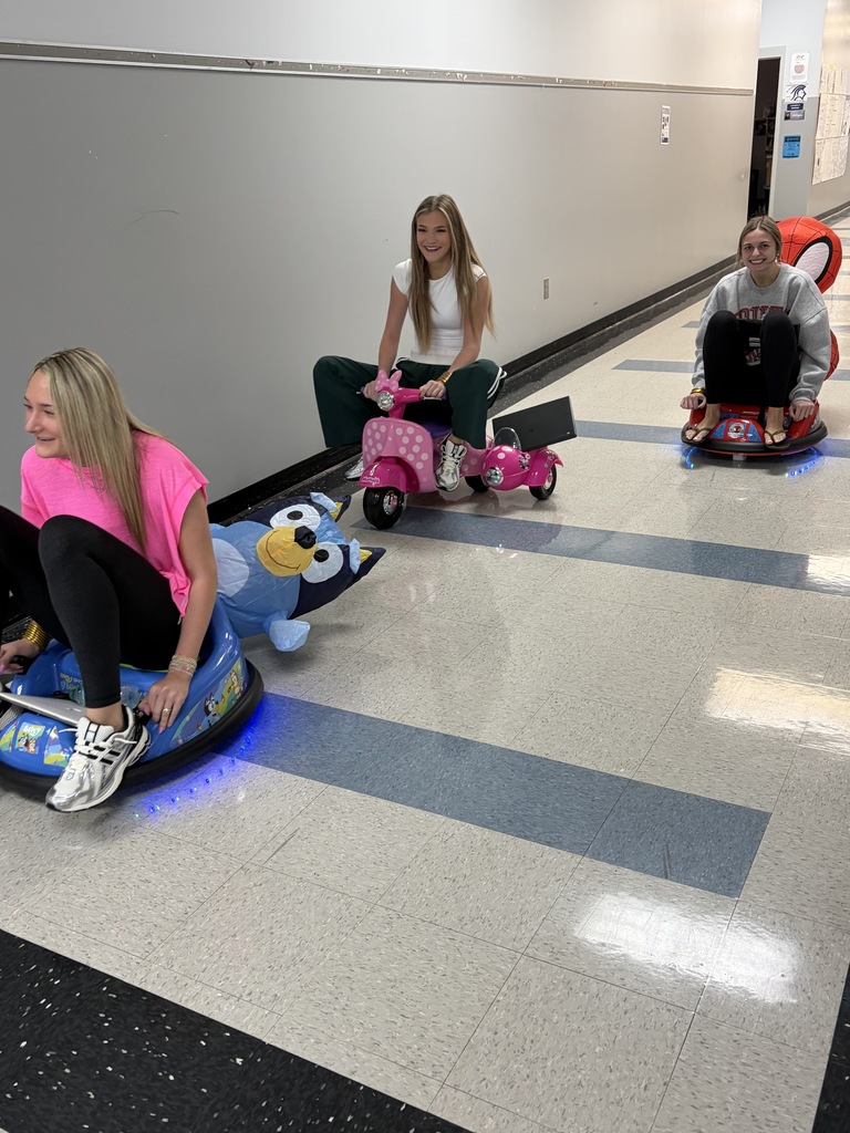 Three people riding scooters on a polished floor with blue lines, one holding a laptop.
