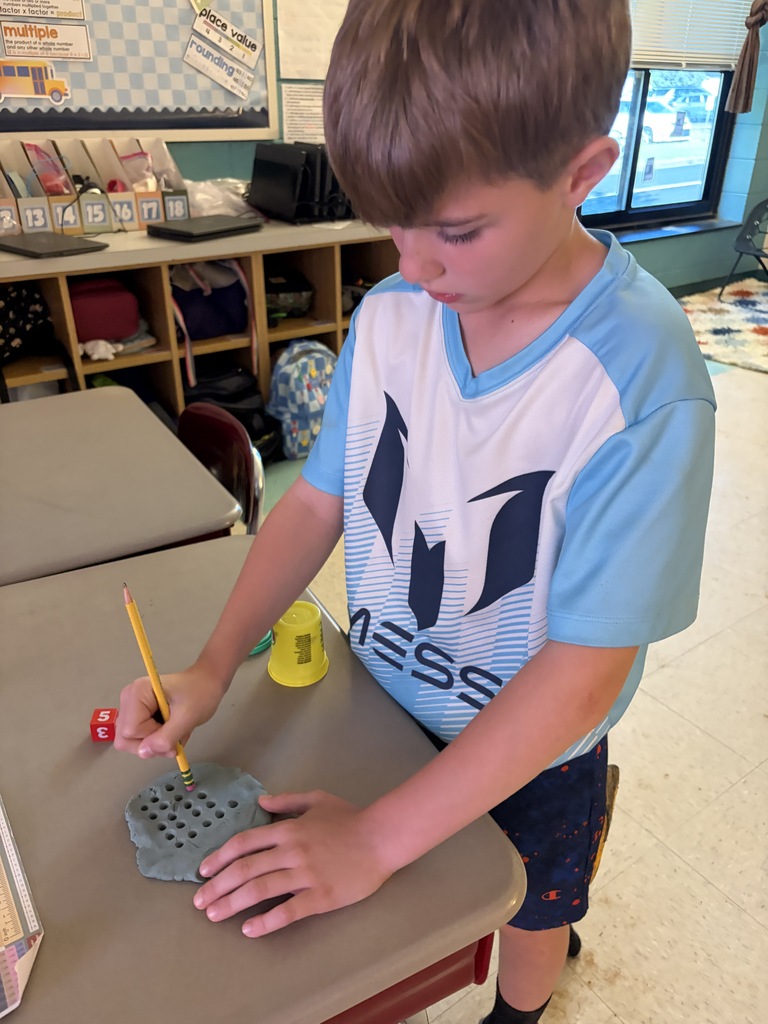 A boy in a blue shirt is using a pencil to carve a design into a piece of clay.