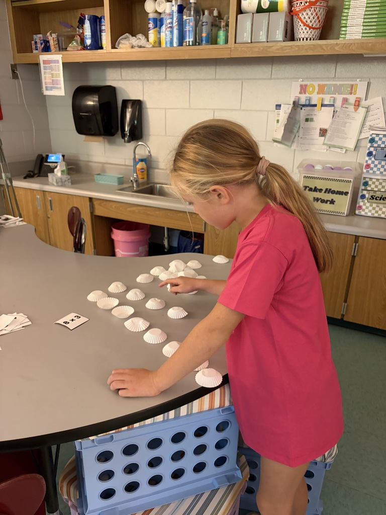A child arranges objects on a table in a classroom with tiled walls and wooden cabinets.