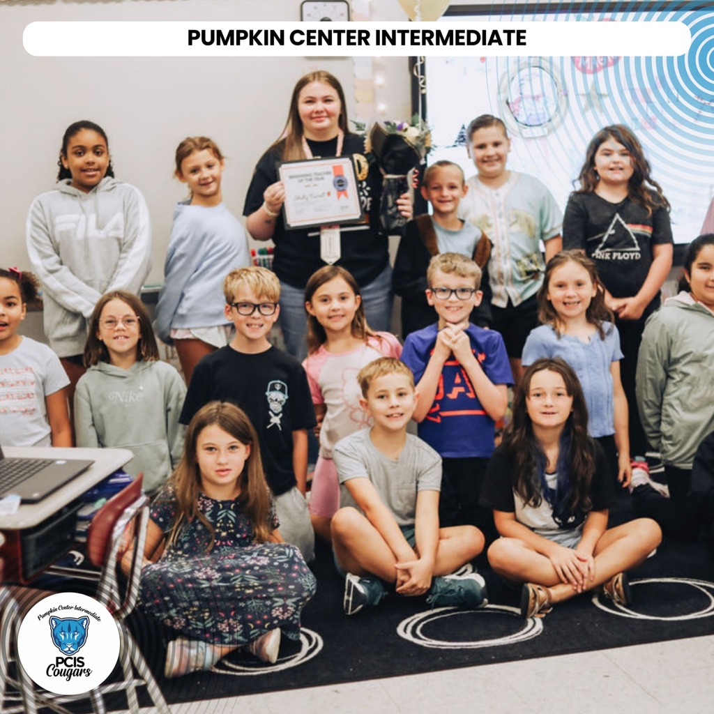 Group of children in a classroom setting, one holding a certificate, seated on the floor.
