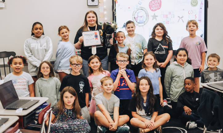 A group of children and an adult woman holding an award stand together in a classroom.