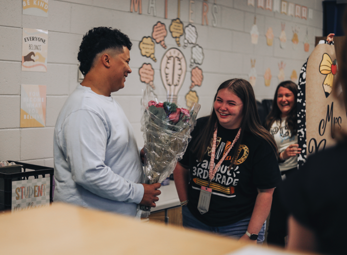 A person with a bouquet of flowers stands beside a woman in a black shirt. They are smiling.