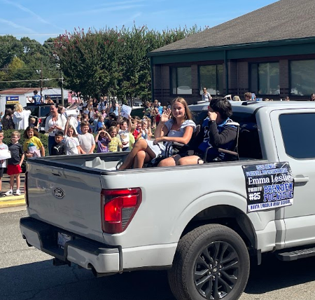 A white pickup truck with two people in the bed. Behind it, a crowd watches.