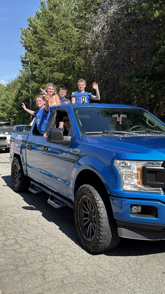 People wave in a blue pickup truck with a person wearing sunglasses in the driver's seat.