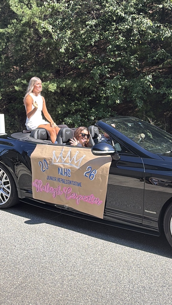 A convertible with a banner reading "20 NHHS Junior Representative 26 Raleigh Corporates." Two people ride inside; one wears sunglasses.