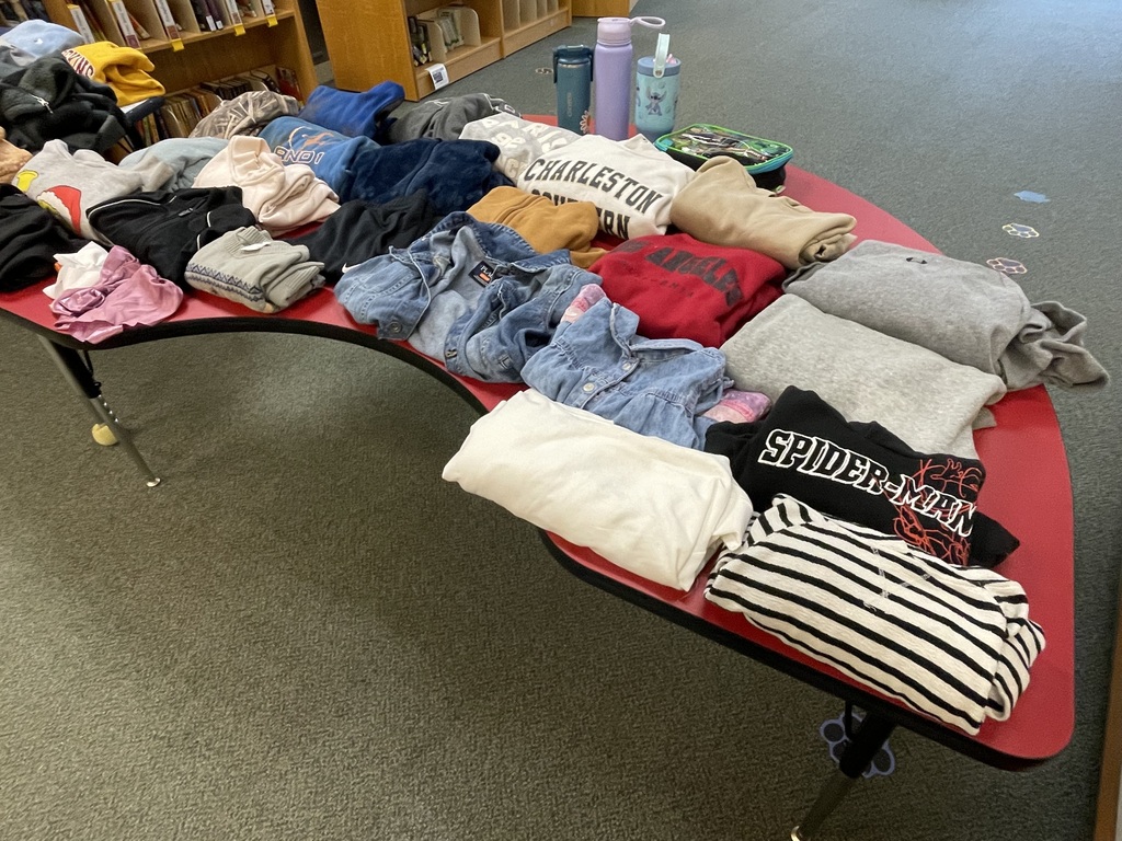 A red table in a room filled with various folded clothes, shelves in background.