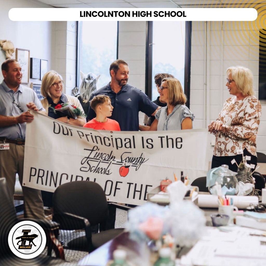 Adults and a child hold a banner reading "Our Principal Is The Principal of the Year."