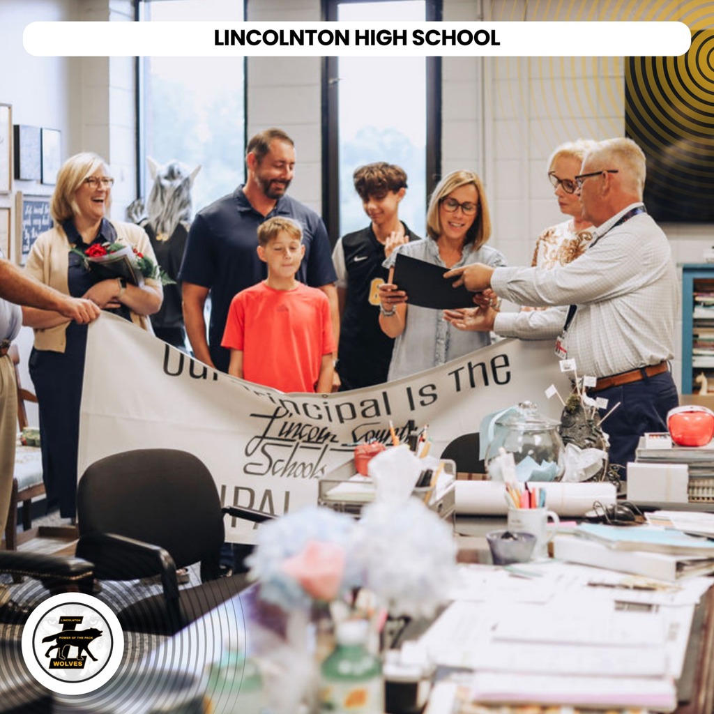People gathered in a room holding a banner reading "Lincolnton High School". A young boy stands at the center.