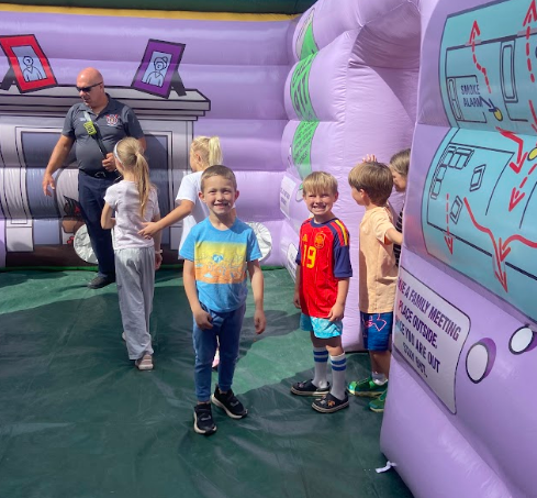 A group of children, one in a blue shirt, stand in front of a large, colorful inflatable play area.